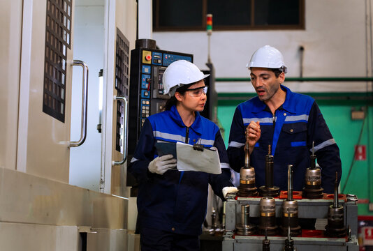 Industrial engineers inspecting cnc machine operation with clipboard in modern factory. ideal for manufacturing, automation, and industry 4.0 marketing campaigns.
