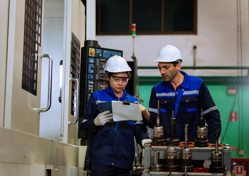 Industrial engineers inspecting cnc machine operation with clipboard in modern factory. ideal for manufacturing, automation, and industry 4.0 marketing campaigns.