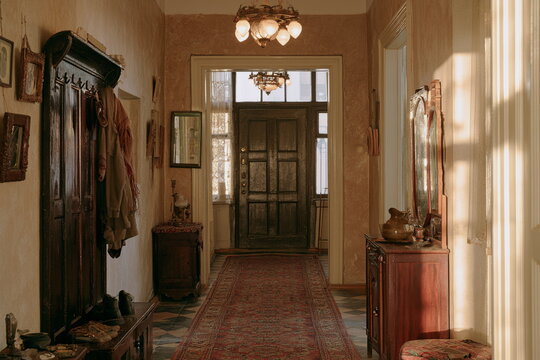 Warm vintage hallway in an old home with a wood door, coat rack, framed art and soft daylight, creating a cozy nostalgic entry with timeless charm.
