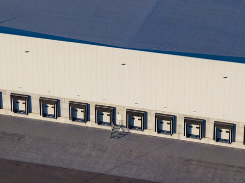 Aerial view of warehouse loading docks with numbered bays and asphalt yard at a logistics distribution center in Genk, Flanders, Belgium.