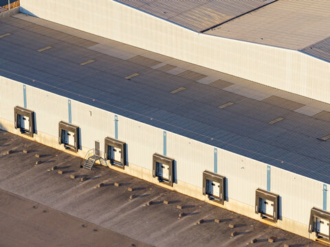 Aerial view of a modern warehouse facility featuring multiple loading docks and a large metal roof in Genk, Flanders, Belgium.