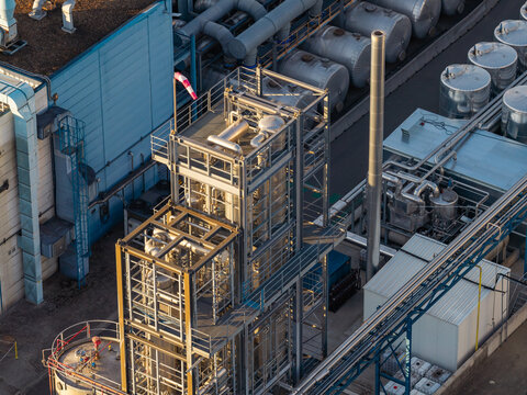 Aerial view of industrial infrastructure with metal storage tanks, complex piping systems, and processing towers at a manufacturing facility in Genk, Flanders, Belgium.