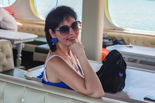 Brunette woman in sunglasses standing on the open deck of cruise ship enjoying ocean views and relaxing vacation travel lifestyle.