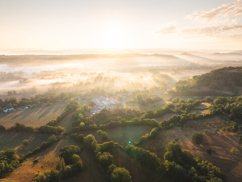 Aerial view of the village of Loubressac nestled in the rolling hills of the Occitanie region at sunrise with morning mist covering the landscape in Loubressac, Occitanie, France.