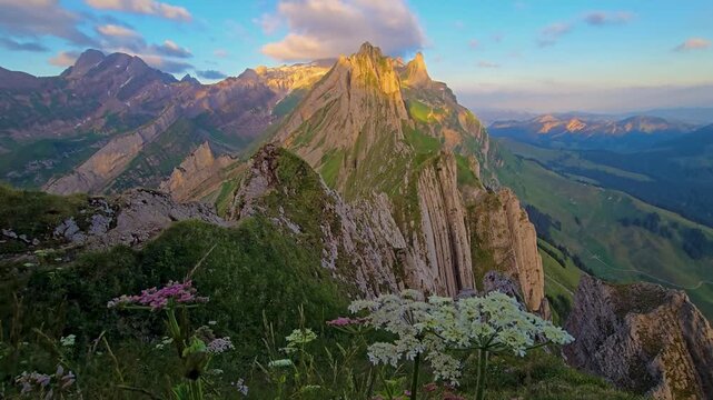 Switzerland showcases the stunning beauty of Schafler Mountain, where vibrant wildflowers dance in the breeze. Experience the tranquil sunset illuminating the majestic peaks.