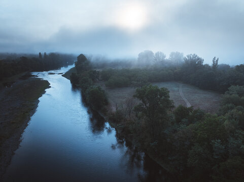 Aerial view of the Dordogne River flowing past the lush greenery and misty trees at Roc Coulon Point de vue in Saint-Sozy, Occitanie, France.