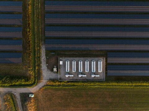 Aerial view of rows of solar panels in a large solar farm with a central power distribution station in the countryside of the Netherlands.