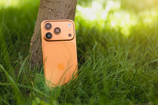 KYIV, UKRAINE - July 10, 2026 : Apple iPhone 17 Pro in Cosmic Orange color stand near tree in green grass.
