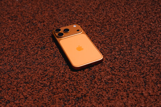 KYIV, UKRAINE - July 10, 2026 : Apple iPhone 17 Pro in Cosmic Orange color on red sport field with artificial rubber surface.