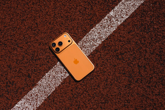 KYIV, UKRAINE - July 10, 2026 : Apple iPhone 17 Pro in Cosmic Orange color on red sport field with artificial rubber surface.