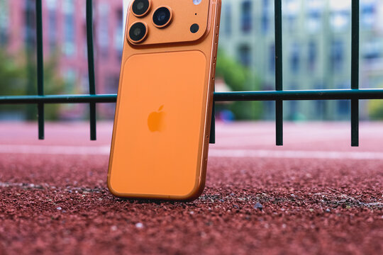 KYIV, UKRAINE - July 10, 2026 : Apple iPhone 17 Pro in Cosmic Orange color leaning against a green wire fence on a red running track, outdoor sport concept.