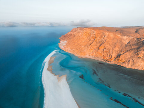 Aerial view of Detwah Lagoon Ramsar Site with turquoise waters, white sandbar, and rugged orange cliffs in Socotra, Yemen.