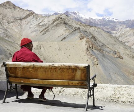 Buddhist monk sitting on bench with Himalaya view in Ladakh, India