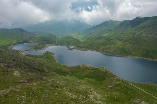 Aerial view of Llyn Llydaw in Eryri National Park surrounded by rugged green mountains and dramatic cloudy skies in Wales, United Kingdom.