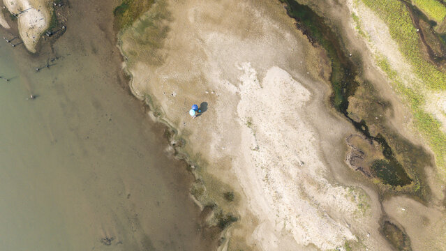 Aerial view of the drought-stricken Po riverbed with exposed sandy banks and two people standing under umbrellas in the heat of summer in Castelvetro Piacentino, Emilia-Romagna, Italy.