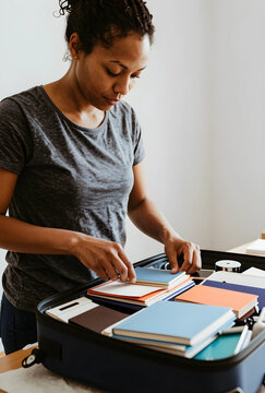 Travel preparation and organization, woman packing colorful notebooks and documents into a suitcase for a trip