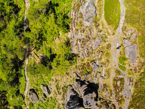 Aerial view of The Roaches rock formation with hiking trails, lush green trees, and rocky terrain in Leek, England, United Kingdom.