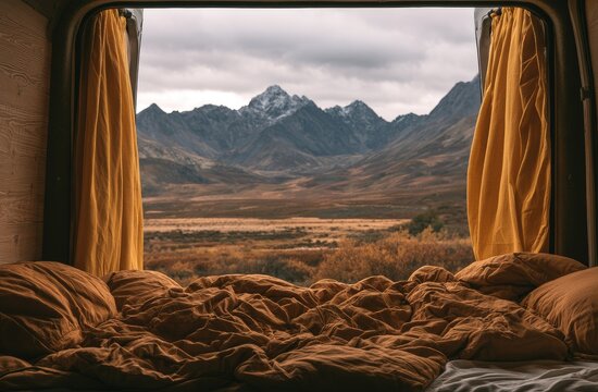 Cozy, rumpled bedding frames a majestic mountain landscape seen from inside