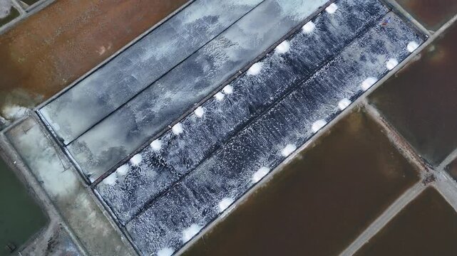 Top-down aerial view of salt evaporation ponds with harvested salt piles on geomembrane