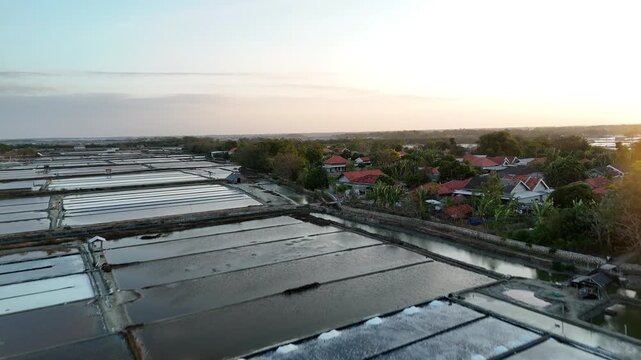 Aerial view of traditional salt fields with harvested salt piles near a rural village at golden hour