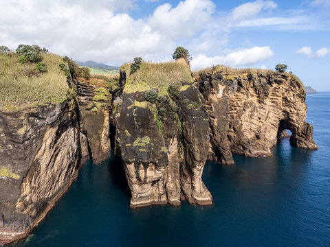 Aerial view of Miradouro do Sertao featuring dramatic volcanic cliffs rising from the deep blue Atlantic Ocean with lush green vegetation in Capelas, Acores, Portugal.