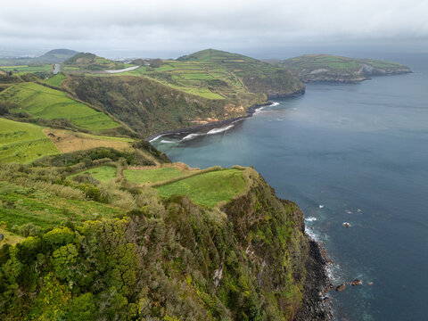 Aerial view of Miradouro de Santa Iria featuring dramatic coastal cliffs, lush green agricultural fields, and the deep blue Atlantic Ocean in Porto Formoso, Acores, Portugal.