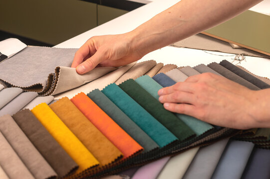Upholstery fabric sample selection on workshop studio table. Hands resting on colorful swatches