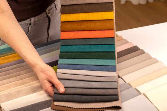 Upholstery fabric swatch fan presentation in open catalog. Designer hands holding stack of soft