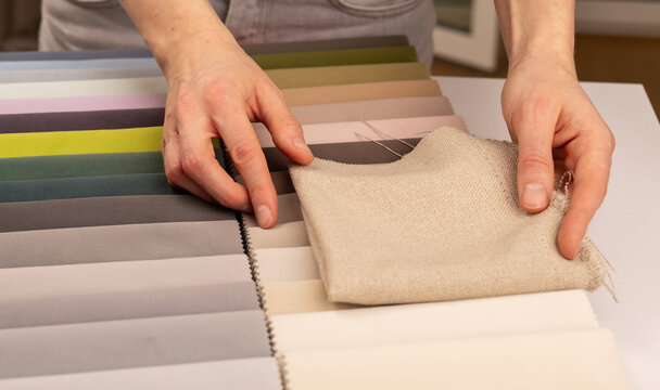 Upholstery fabric swatch selection on studio workshop table. Interior designer hands holding light