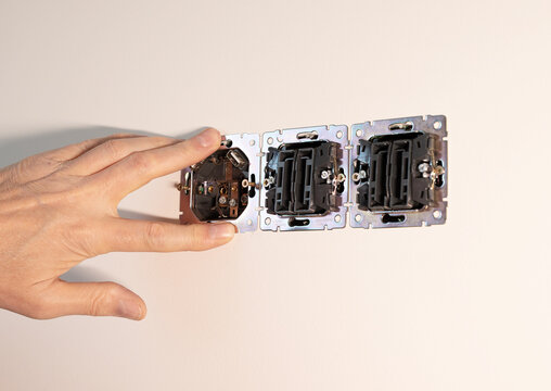 Wall socket installation in plaster wall panel by electrician. Hands adjusting metal triple