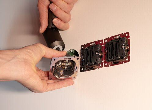 Wall socket installation using electric screwdriver tool in room. Electrician mounting black power