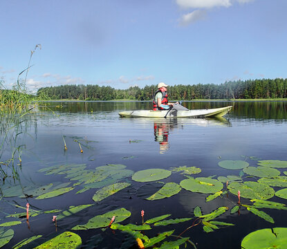 Woman paddler in vest steers kayak across calm lake water. Female kayaker row boat near green