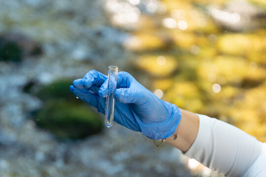 person in blue gloves holding glass tube with water sample outdoors testing for escherichia coli and gastrointestinal disease outbreak risk with copy space for banner design