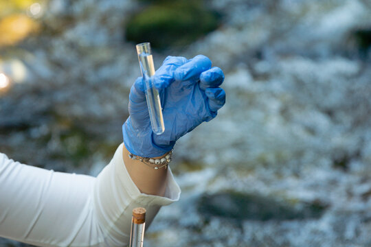 person in blue gloves holding glass tube with water sample outdoors testing for escherichia coli and gastrointestinal disease outbreak risk with copy space for banner design