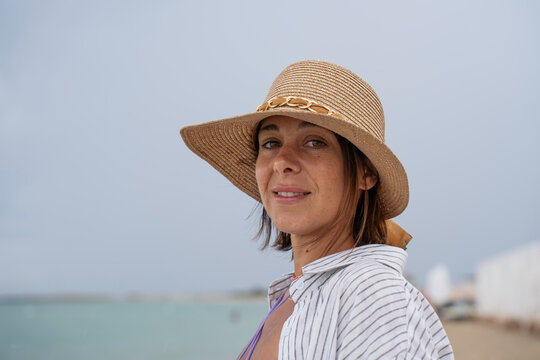 Relaxed woman enjoying a sunny beach getaway in a straw hat. Natural summer portrait by turquoise water with a peaceful vacation mood.