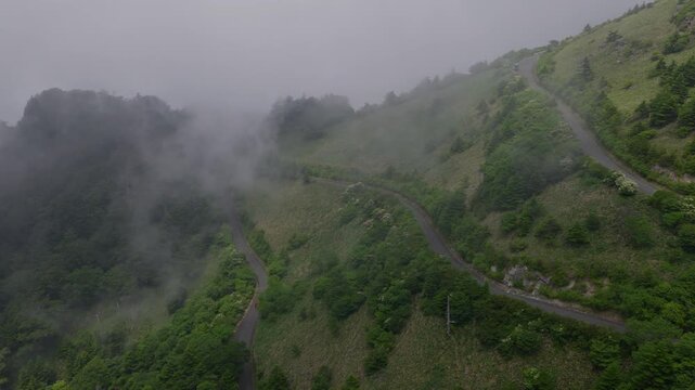 Flying over car driving winding mountain road with fog and clouds