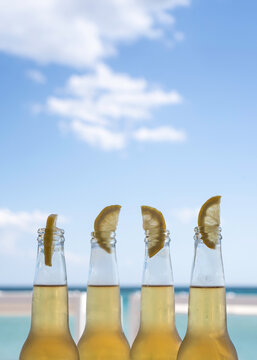 Against a bright blue sky, four chilled beer bottles with lemon wedges create a clean summer still life. Vertical seaside composition with generous copy space suits book covers and beverage ads.
