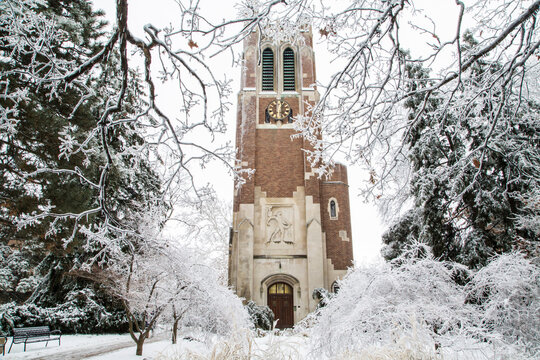 East Lansing, Michigan, United States - 23 December 2013: View of Beaumont Tower at Michigan State University surrounded by snow-covered trees and branches on a winter day.