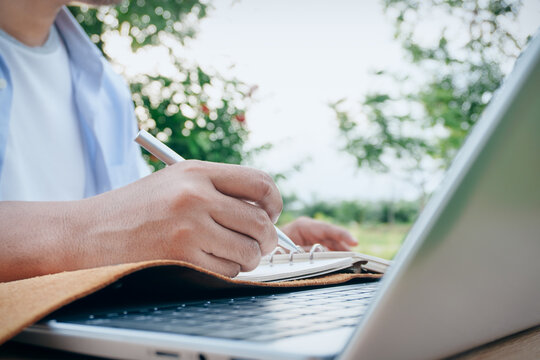 Business Professional Writing Notes in Notebook Beside Laptop Computer, Natural Outdoor Workspace, Concept of Strategic Planning, Productivity, Remote Work, Education, Organization, Digital Lifestyle