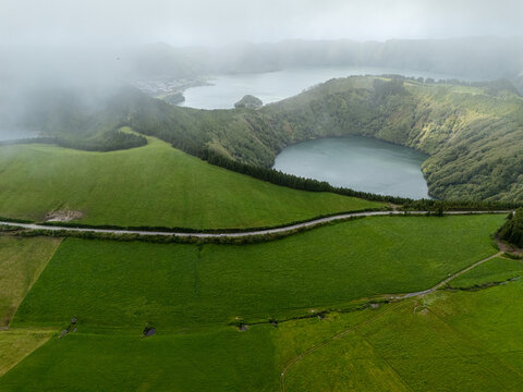 Aerial view of Sete Cidades caldera with its iconic twin lakes surrounded by lush green volcanic hills and misty clouds in Azores, Portugal.