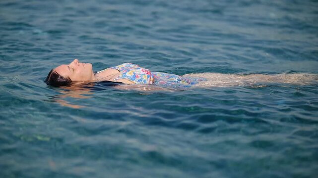 Young Woman Relaxing and Floating Backwards on Water Surface in Pool