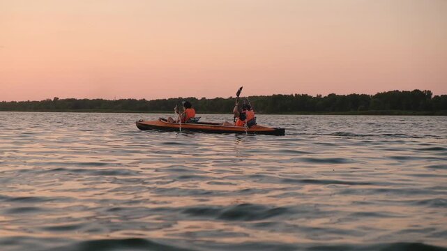 Two People Kayaking on Calm Lake During Orange Sunset Silhouette View