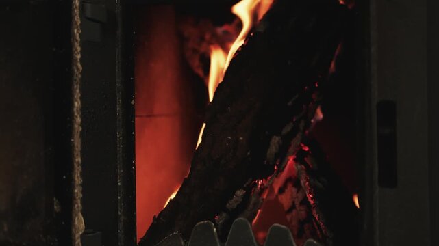 First-person view of hands opening a metal stove door, revealing glowing logs and flames inside.