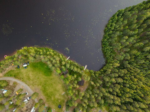 Aerial view of Jukajarvi lake shoreline with dense pine forest, small cabins, and a gravel parking area in Juva, South Savo, Finland.