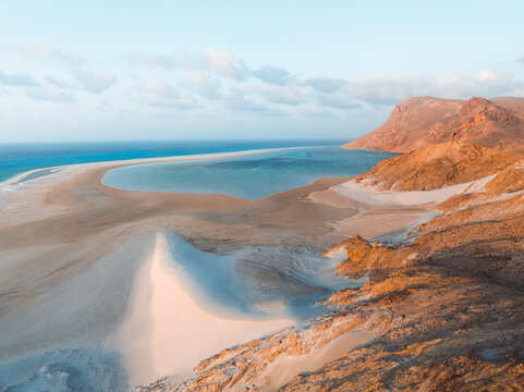 Aerial view of Detwah Lagoon Ramsar Site with white sand dunes, turquoise waters, and rocky mountains in Socotra, Yemen.