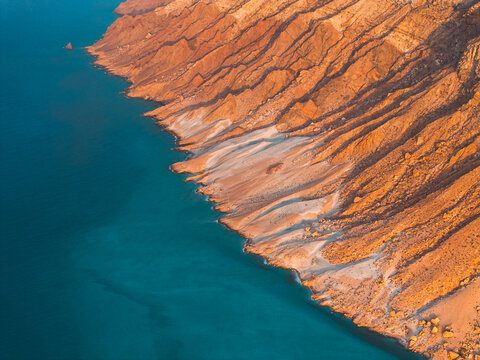 Aerial view of Detwah Lagoon Ramsar Site with its turquoise waters meeting dramatic rugged cliffs and sandy shoreline in Socotra, Yemen.