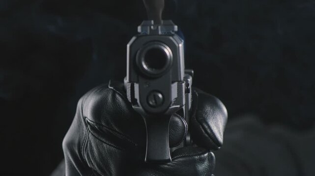 Hand with black glove holding a smoking gun pointed at the camera with pure black landscape background