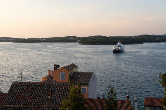 View of the beautiful coastal town of Rovinj, Croatia, with its characteristic red-tiled roofs overlooking the Adriatic Sea, and a cruise ship in the distance.