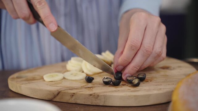 Woman slicing blueberries on a wooden cutting board close up