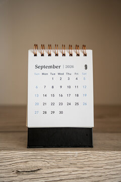 Small spiral desk calendar showing September 2026 dates standing on a wooden surface indoors